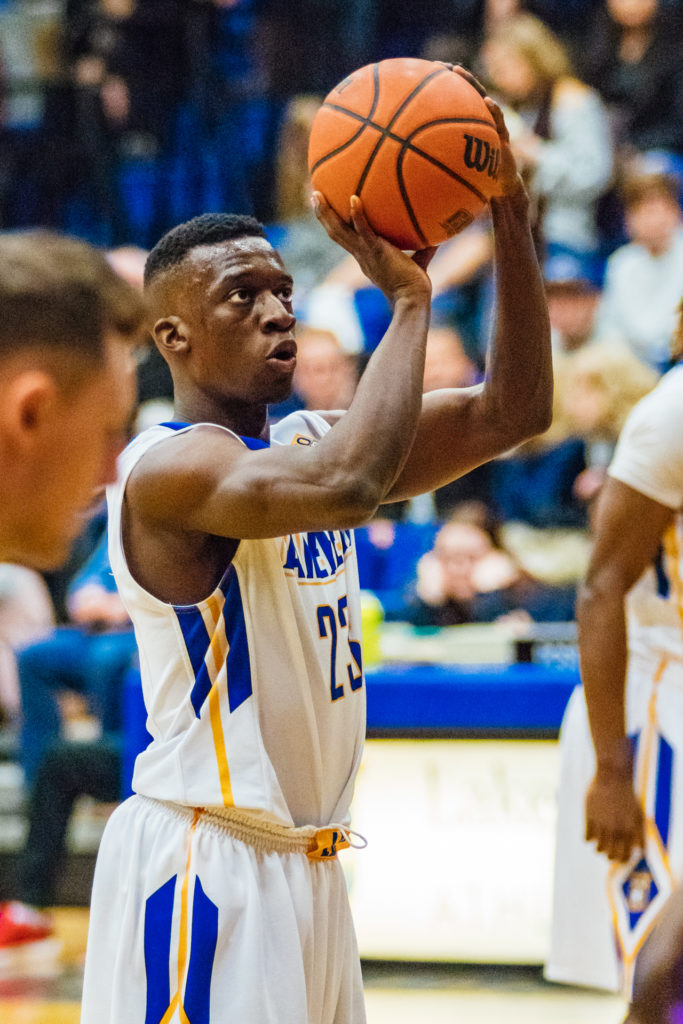 An energetic sports photograph capturing a Lakehead University basketball player in mid-action, focused on shooting a free throw. The high-clarity shot features a shallow depth of field, highlighting the athlete's concentration against a blurred, engaged crowd in a Thunder Bay gymnasium.