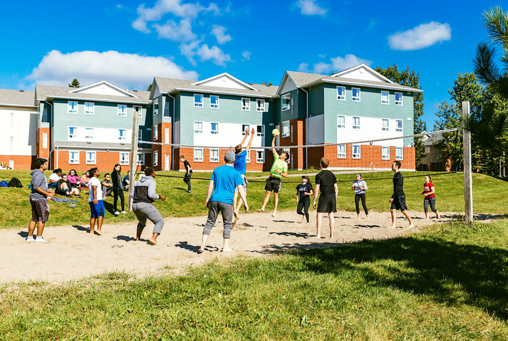 Lakehead University students playing sand volleyball in front of campus residence buildings; candid student life and outdoor recreation photography in Thunder Bay.