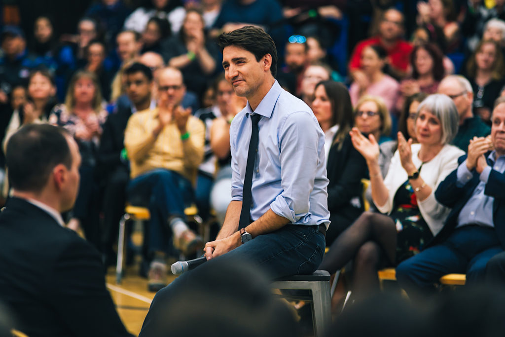 Justin Trudeau seated on a stool during a town hall meeting in Thunder Bay; candid political photography with a blurred audience.