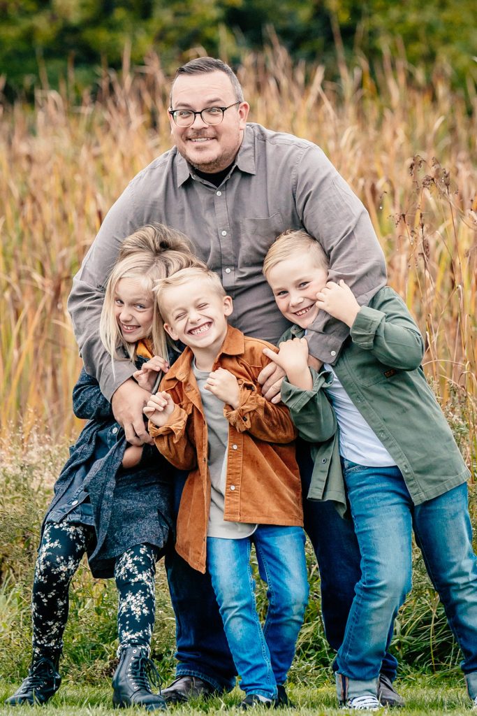 portrait of a father and three children sharing a moment of genuine laughter and connection. The high-clarity shot features natural skin tones and a soft depth of field against a vibrant autumnal background in Thunder Bay , reflecting TbayAlive’s focus on authentic storytelling and genuine family interactions.