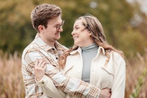 A portrait of a young couple sharing a playful look and warm embrace at Friendship Gardens in Thunder Bay. The high-clarity shot features natural skin tones and soft, modern lighting against a vibrant autumnal backdrop, reflecting TbayAlive’s focus on authentic storytelling and capturing the genuine connection between individuals in the local community.