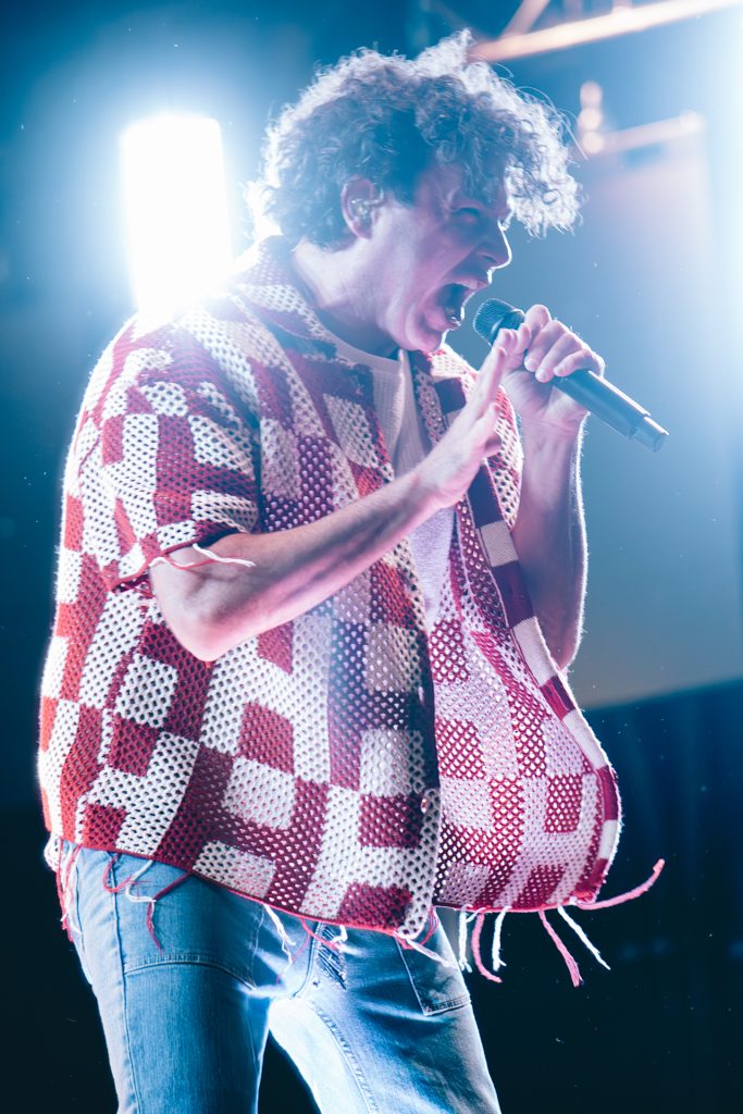 An energetic and emotionally expressive concert photograph of a male vocalist performing under intense, high-contrast stage lighting in a Thunder Bay venue; the atmospheric shot utilizes dramatic backlighting to highlight movement and raw energy, reflecting TbayAlive’s signature storytelling and decade-plus experience documenting live music.