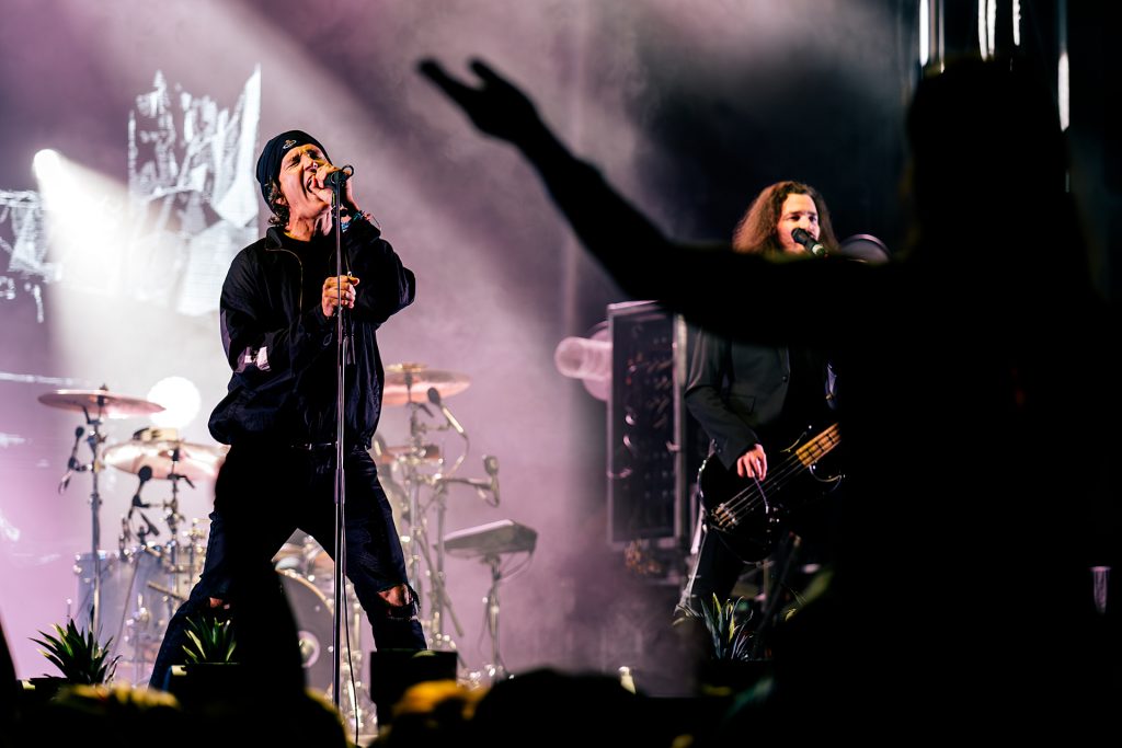 An energetic, high-contrast concert photograph of a male vocalist performing with intense emotion under atmospheric stage lighting ; the shot utilizes dramatic backlighting and silhouettes to capture the raw power of the live music scene in Thunder Bay, reflecting TbayAlive’s signature storytelling and decade-plus experience documenting local and touring acts.