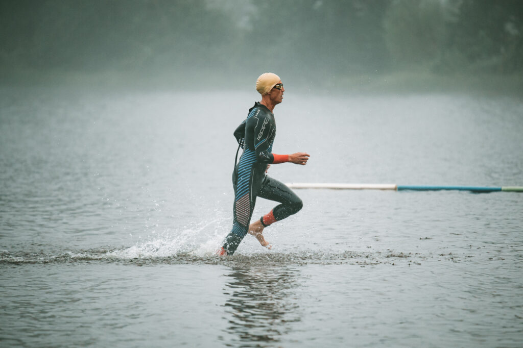 Triathlon athlete in a wetsuit and swim cap running out of the water during a race, Thunder Bay sports photography