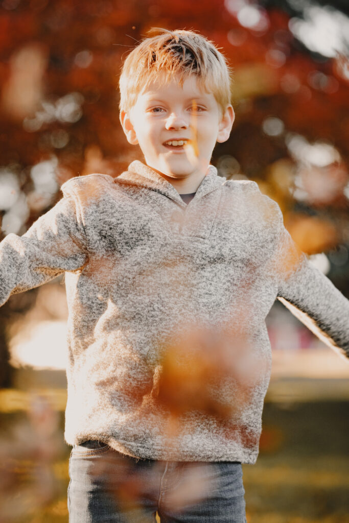 Child portrait of a red-haired boy smiling outdoors in a grey hoodie with warm autumn foliage bokeh in the background, Thunder Bay