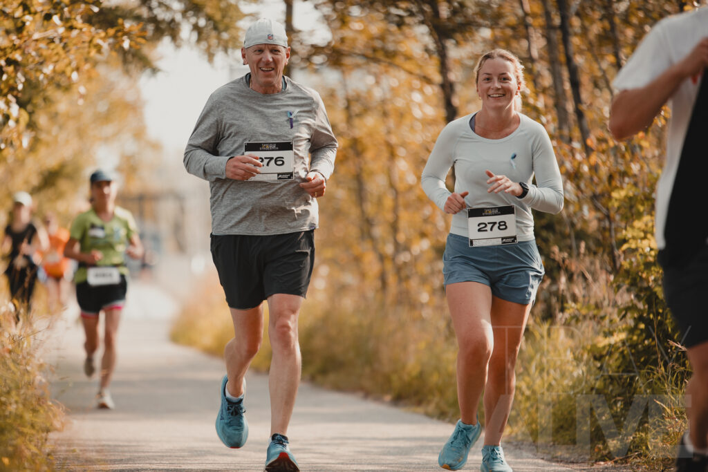 Two smiling runners with race bibs competing in a road race through fall foliage in Thunder Bay, sports event photography