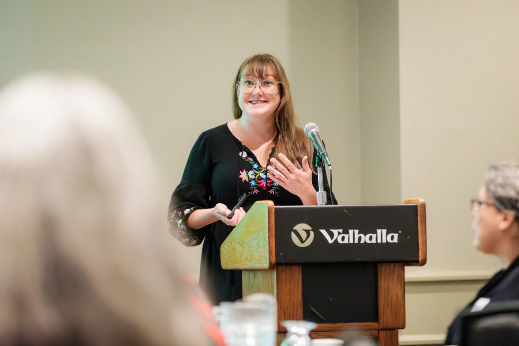 Woman speaking at a Valhalla podium during a corporate or community event in Thunder Bay, smiling and gesturing at the microphone