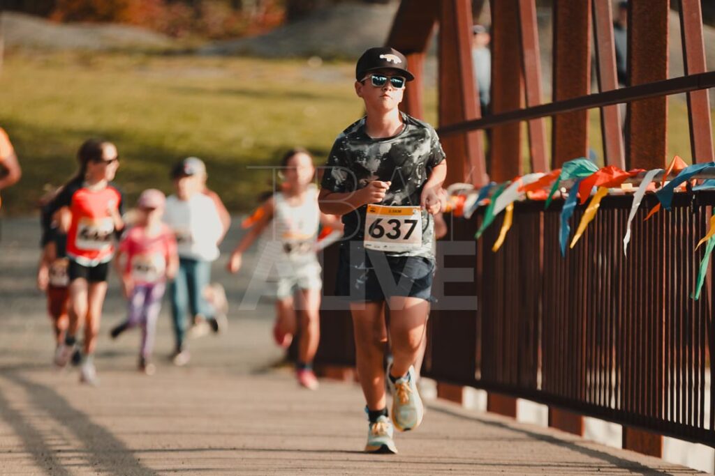 Runner with bib number 637 racing across a decorated bridge during a Thunder Bay road race, with other runners in the background